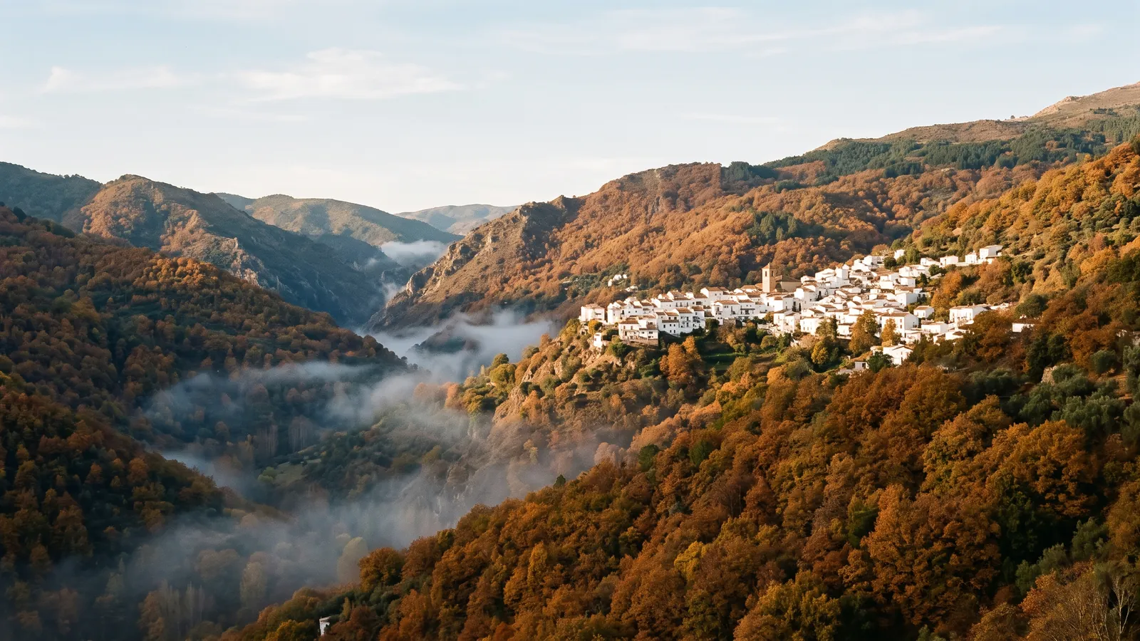 Mountain valley in autumn with copper chestnut forests and a white village on the hillside