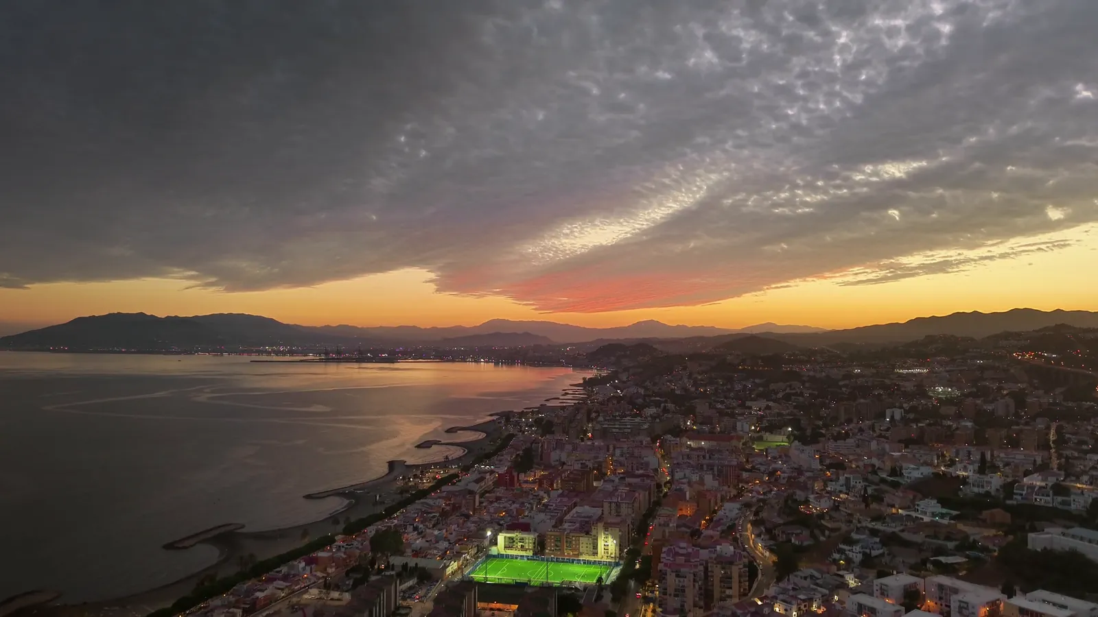 Aerial view of the Málaga coast at sunset with the city lights and mountains in the background